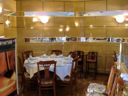 Comedor de restaurante con mesa preparada. Paredes revestidas de madera, sillas con cojines florales e iluminación cenital.