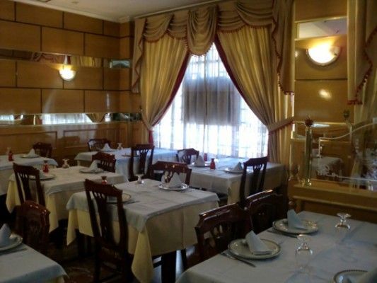 Interior del restaurante: Mesas con mantelería blanca. Sillas de madera. Paredes y cortinas doradas.