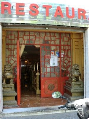 Entrada de restaurante chino de temática roja con puertas decorativas, estatuas y puerta abierta.