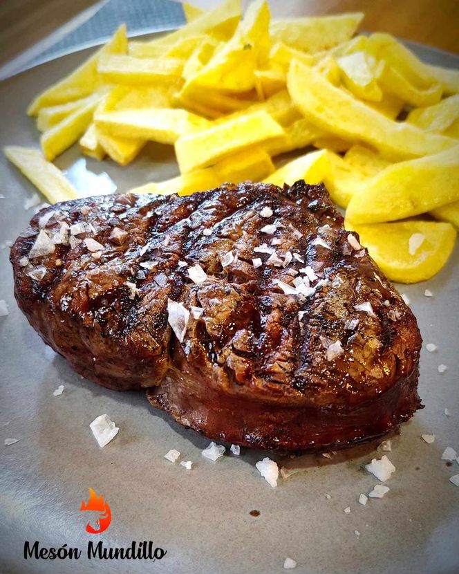 Un primer plano de un bistec y papas fritas en un plato.