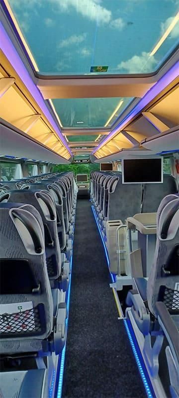 Das Innere eines Busses mit vielen Sitzen und einem Fernseher an der Decke.