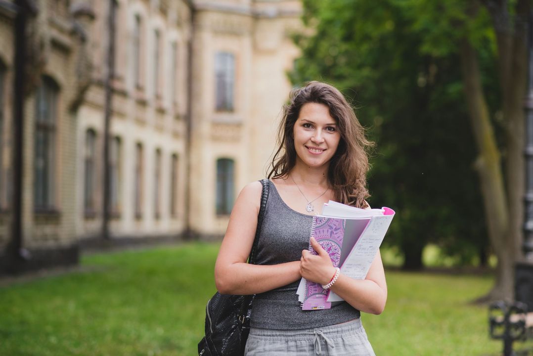 Una mujer está parada frente a un edificio sosteniendo un libro.