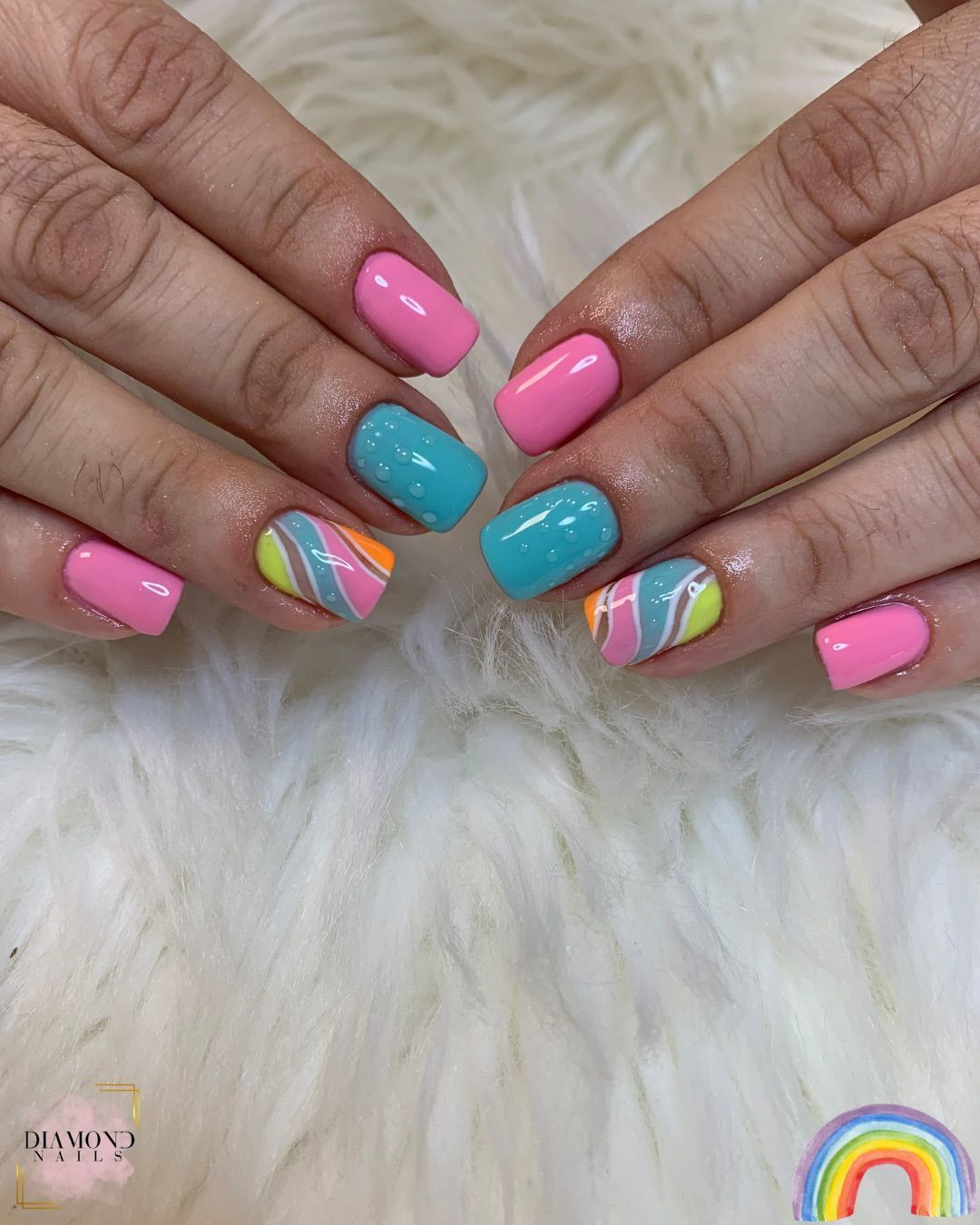 Manos con uñas cortas y cuadradas pintadas de color rosa y turquesa, algunas con diseños abstractos coloridos.