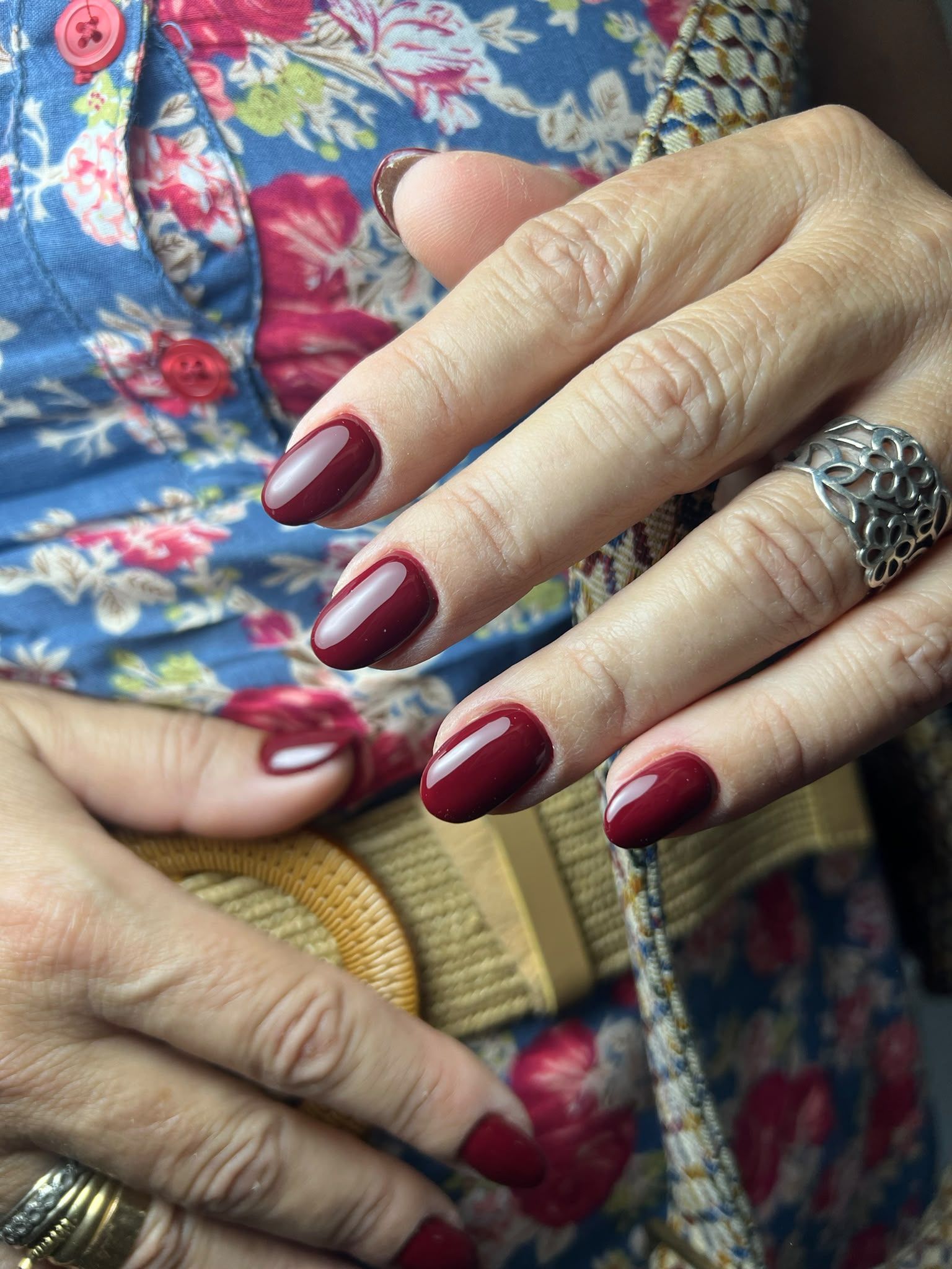 Manos con uñas color burdeos y anillos ornamentados apoyadas sobre una tela estampada.