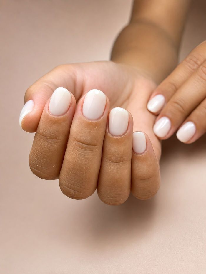 Mano con uñas largas, ovaladas y de color nude, una de ellas con brillo dorado.
