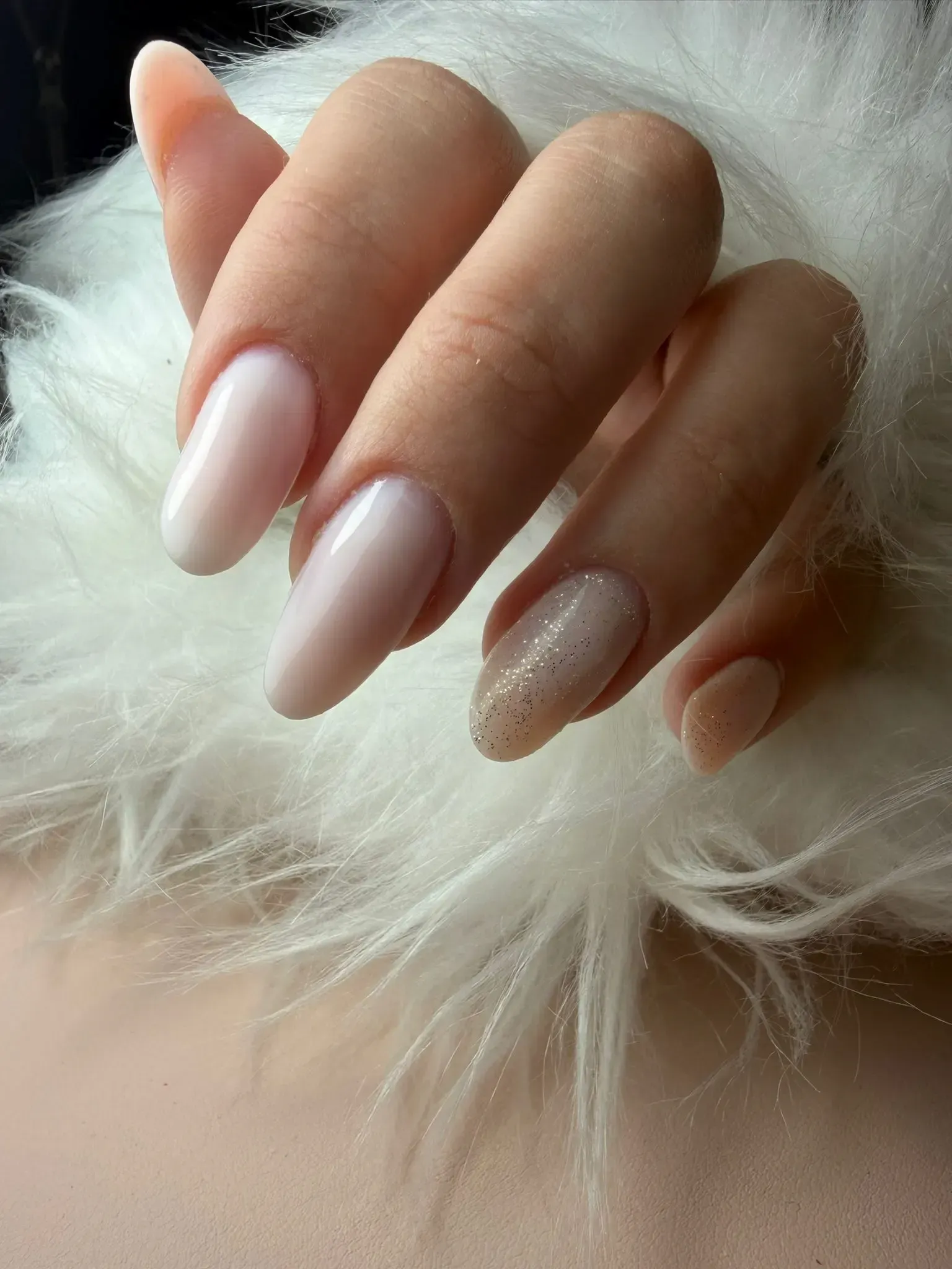 Mano con uñas largas en forma de almendra pintadas de color rosa nude, una de ellas con brillantina.