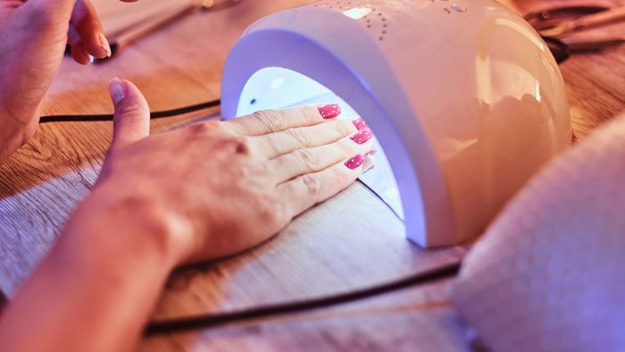Mano con esmalte de uñas rojo bajo una lámpara de uñas UV, en el interior.