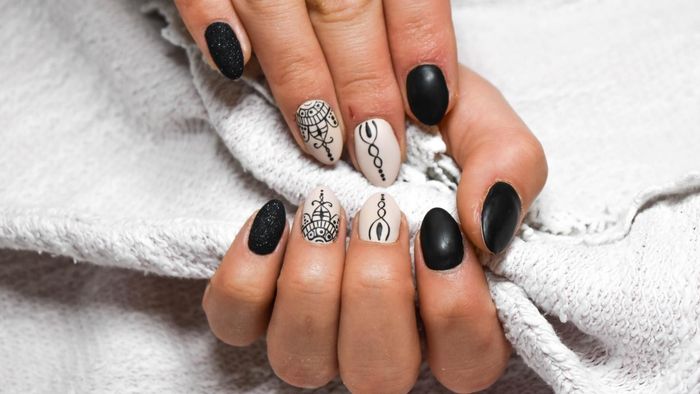 Manos con uñas en forma de almendra, algunas pintadas con brillantina y diseños de copos de nieve rojos.