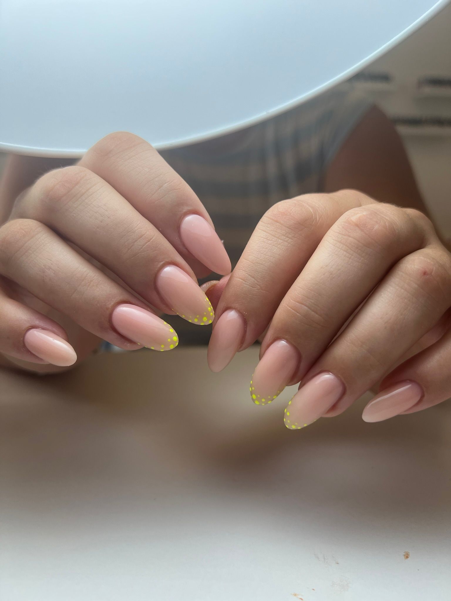 Manos con uñas en forma de almendra pintadas de color nude con puntas de cuentas amarillas.