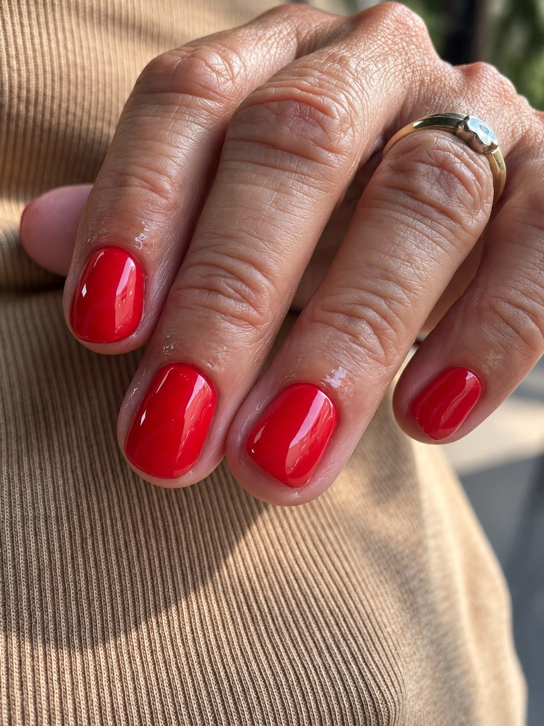 Mano con manicura de color rojo intenso apoyada sobre una tela beige, con un anillo de plata