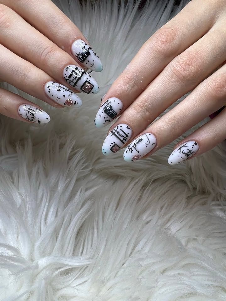 Uñas blancas en forma de almendra con diseño en negro y marrón sobre un fondo blanco difuso.