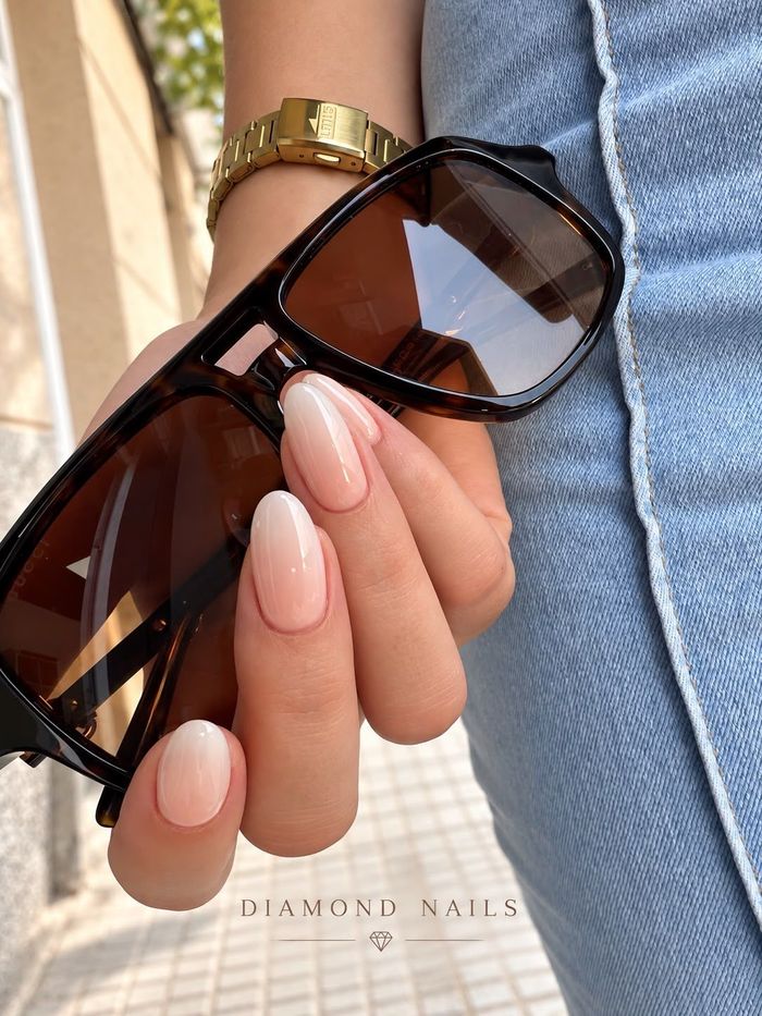Manos con uñas ovaladas de color rosa claro con puntas adornadas con cuentas amarillas.