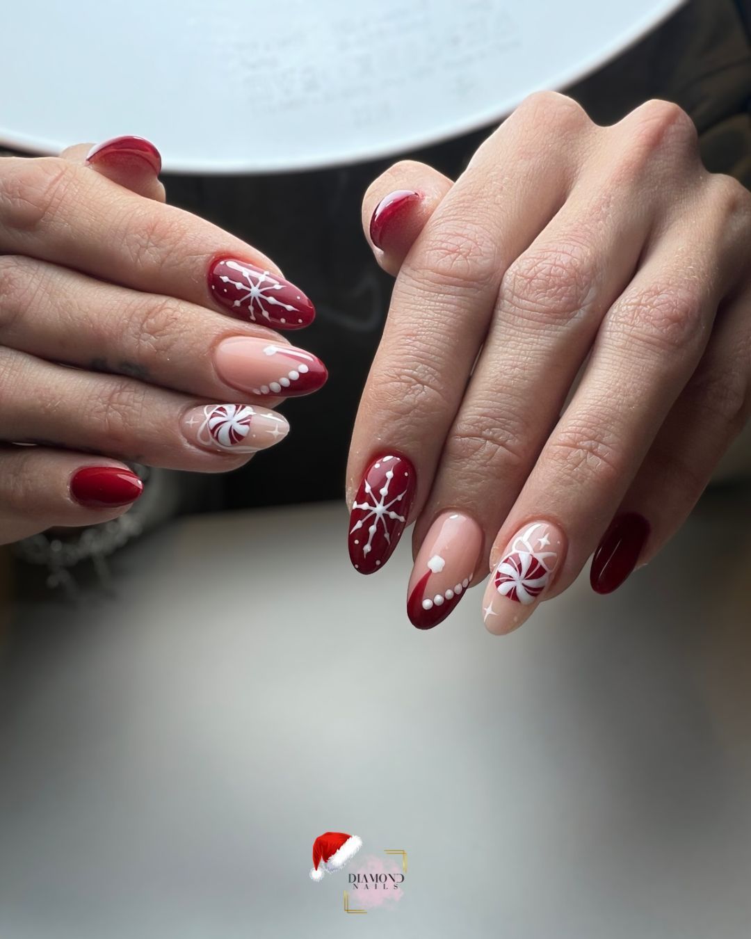 Uñas almendradas en tonos rojos y nude con diseños de copos de nieve y puntos blancos, una manicura festiva.