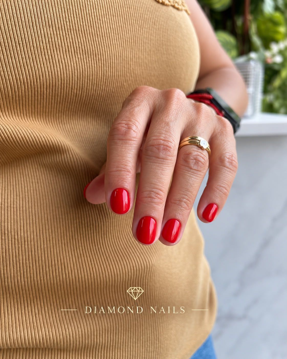 Mano con uñas rojas brillantes y un anillo dorado apoyada sobre un top beige de canalé
