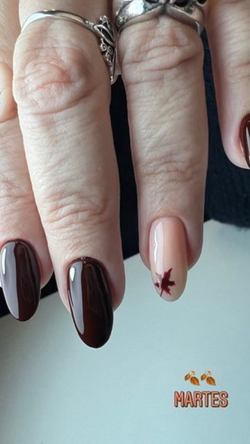 Primer plano de una mano con uñas ovaladas, de color marrón oscuro y rosa claro, con un pequeño diseño de hojas.