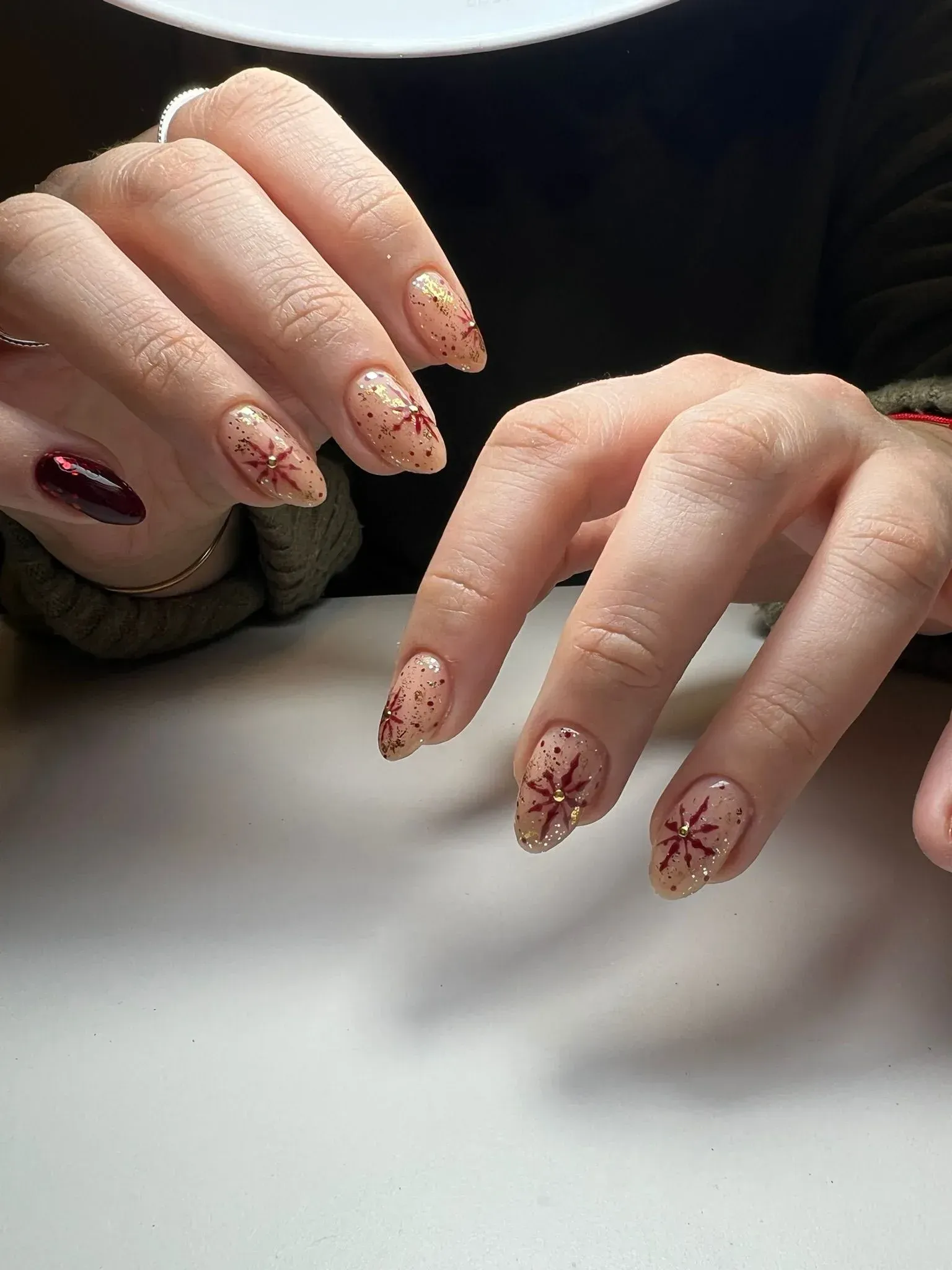 Manos con uñas en forma de almendra, algunas pintadas con brillantina y diseños de copos de nieve rojos.
