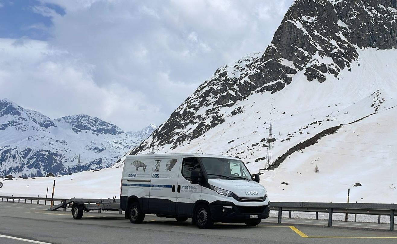Ein weisser Lieferwagen parkt am Hang eines schneebedeckten Berges.