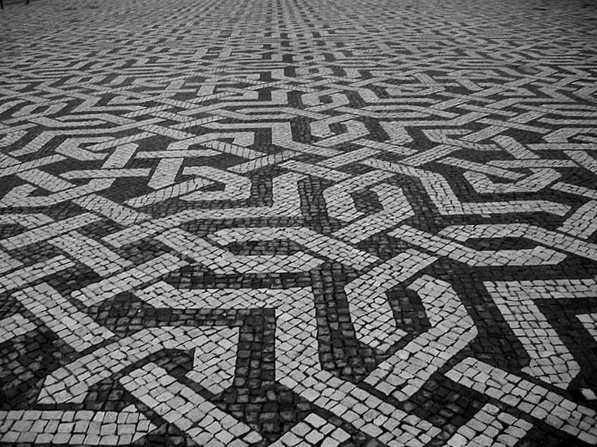 Calçada de paralelepípedos pretos e brancos com um padrão de encaixe complexo.