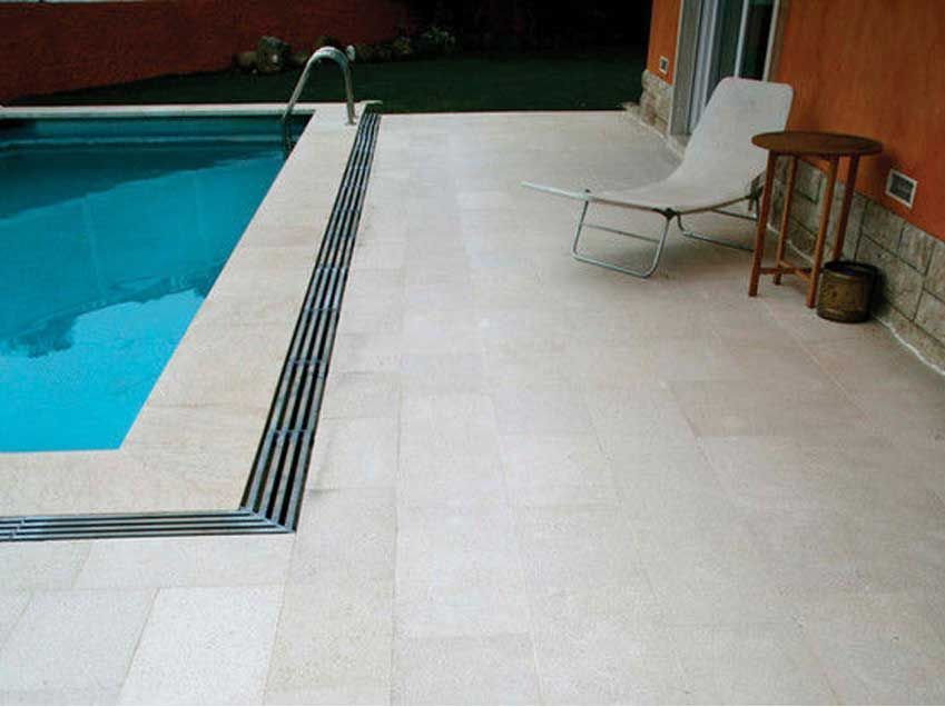 Pátio junto à piscina com piscina, espreguiçadeira, mesa e parede de terracota.