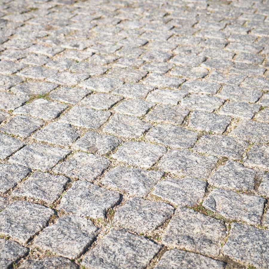 Caminho de paralelepípedos, com pedras cinzentas dispostas em um padrão repetitivo.