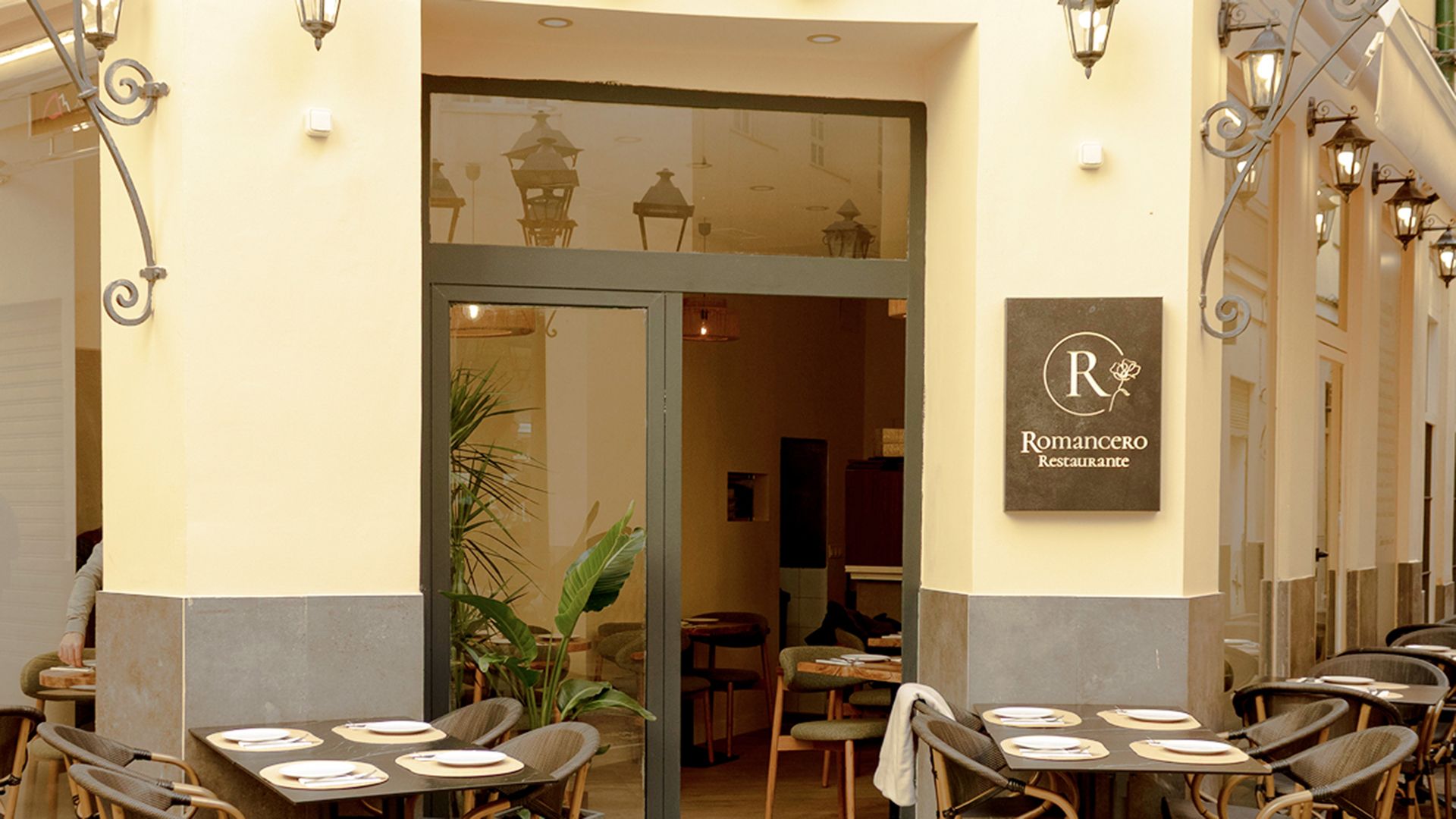 Entrada del restaurante con mesas al aire libre, con un cartel que dice