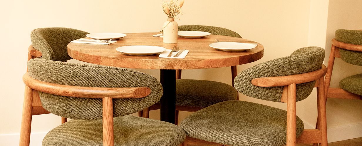 Mesa de comedor redonda de madera con cuatro sillas. Las sillas tienen tapizado de tela verde y estructura de madera.