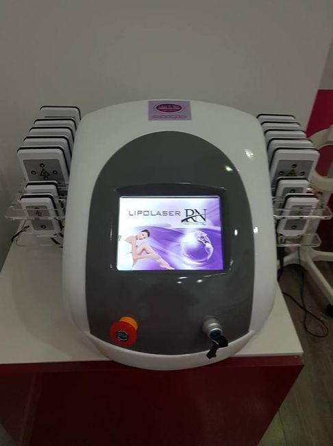 Máquina de lipoláser con electrodos blancos y grises sobre una superficie roja. La pantalla muestra una imagen.
