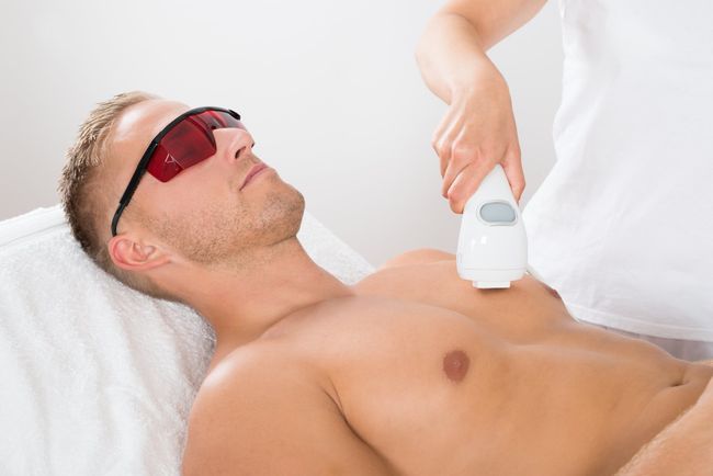 Hombre recibiendo tratamiento de depilación láser en el pecho; lleva gafas de seguridad, en un spa.