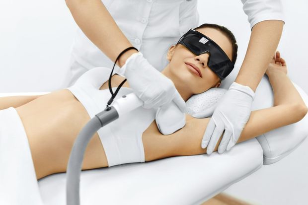 Mujer recibiendo depilación láser en las axilas en una clínica, con gafas protectoras.