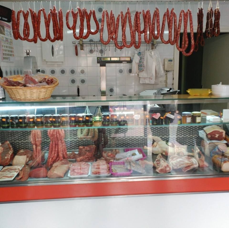 Vitrina de carnicería con diversas carnes y embutidos colgantes.