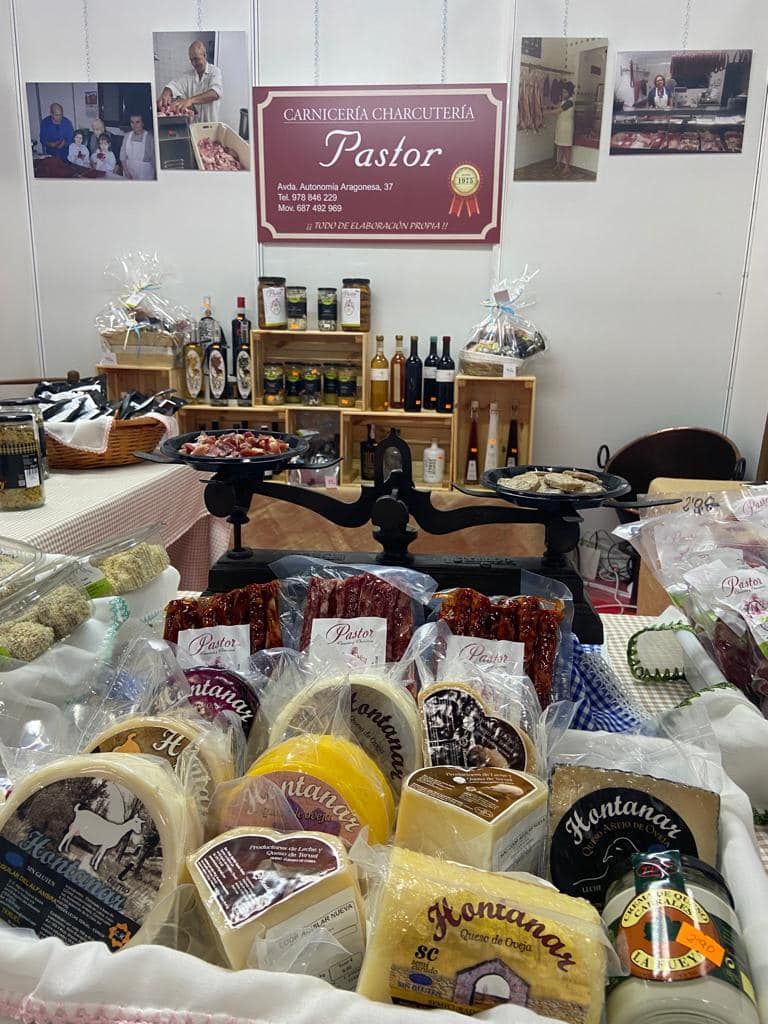 Un puesto de comida con quesos y carnes, con vinos, aceites y un cartel que dice