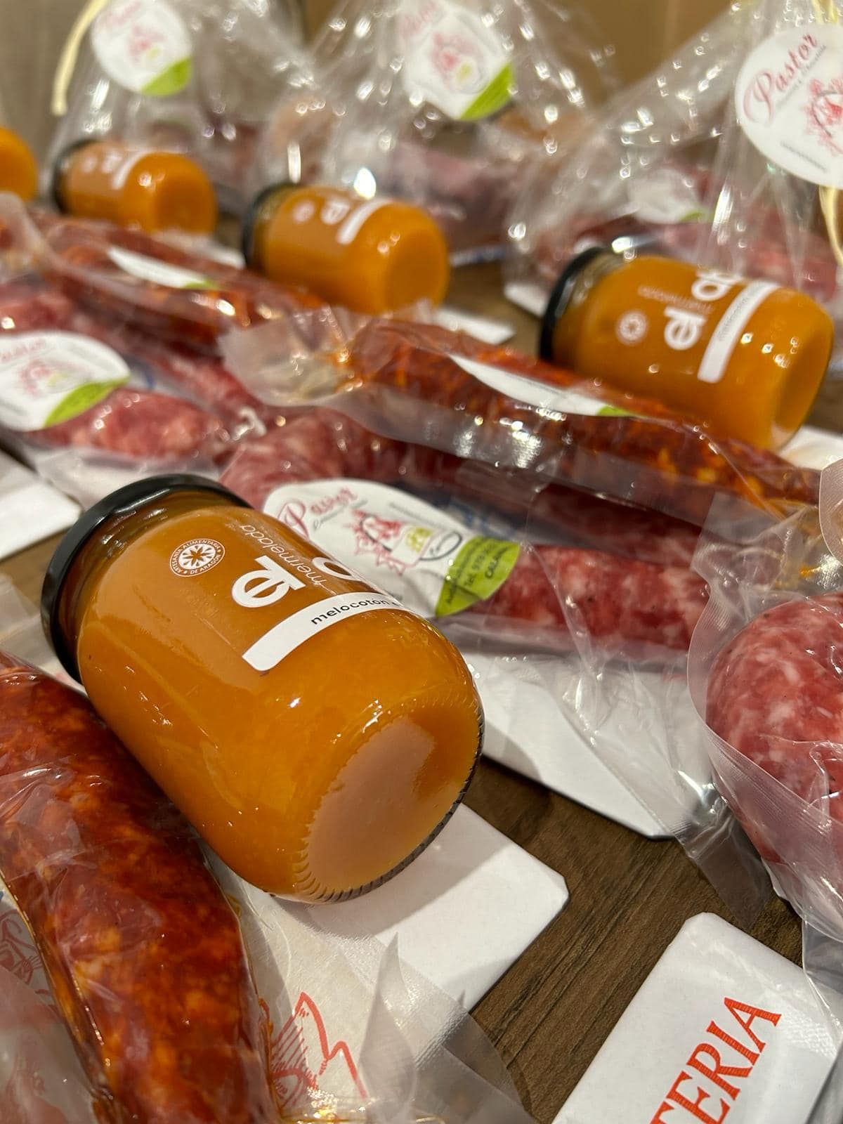 Tarros de líquido de naranja y embutidos diversos, envasados al vacío, sobre una superficie de madera.