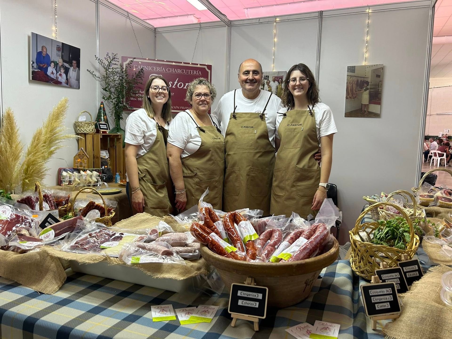 Gente en un puesto de comida vendiendo embutidos. Con caras sonrientes con delantales están detrás de una mesa con productos.