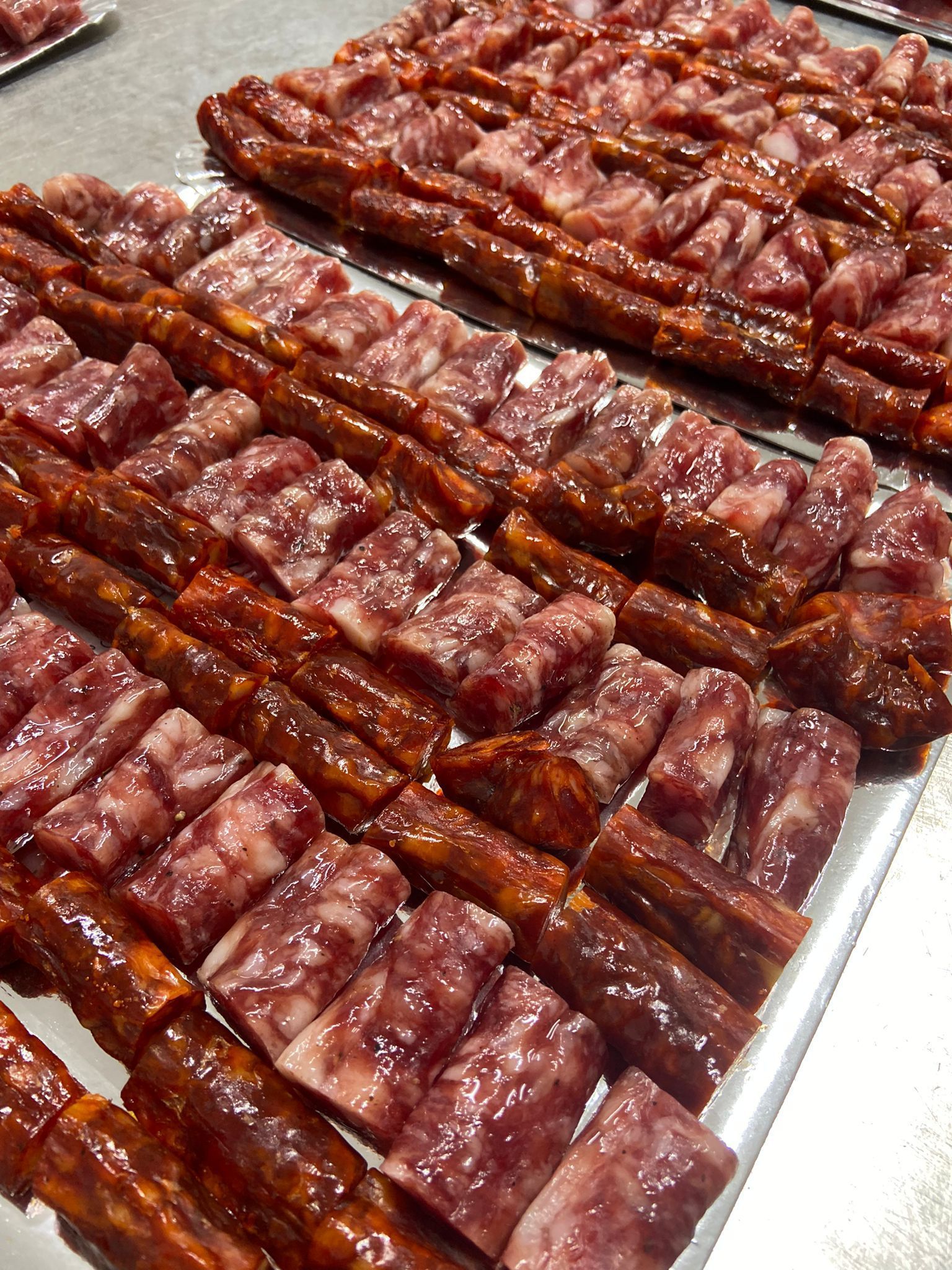 Rebanadas de salchicha dispuestas en filas sobre una bandeja metálica. Las salchichas son de color rojizo y rojo rosado.