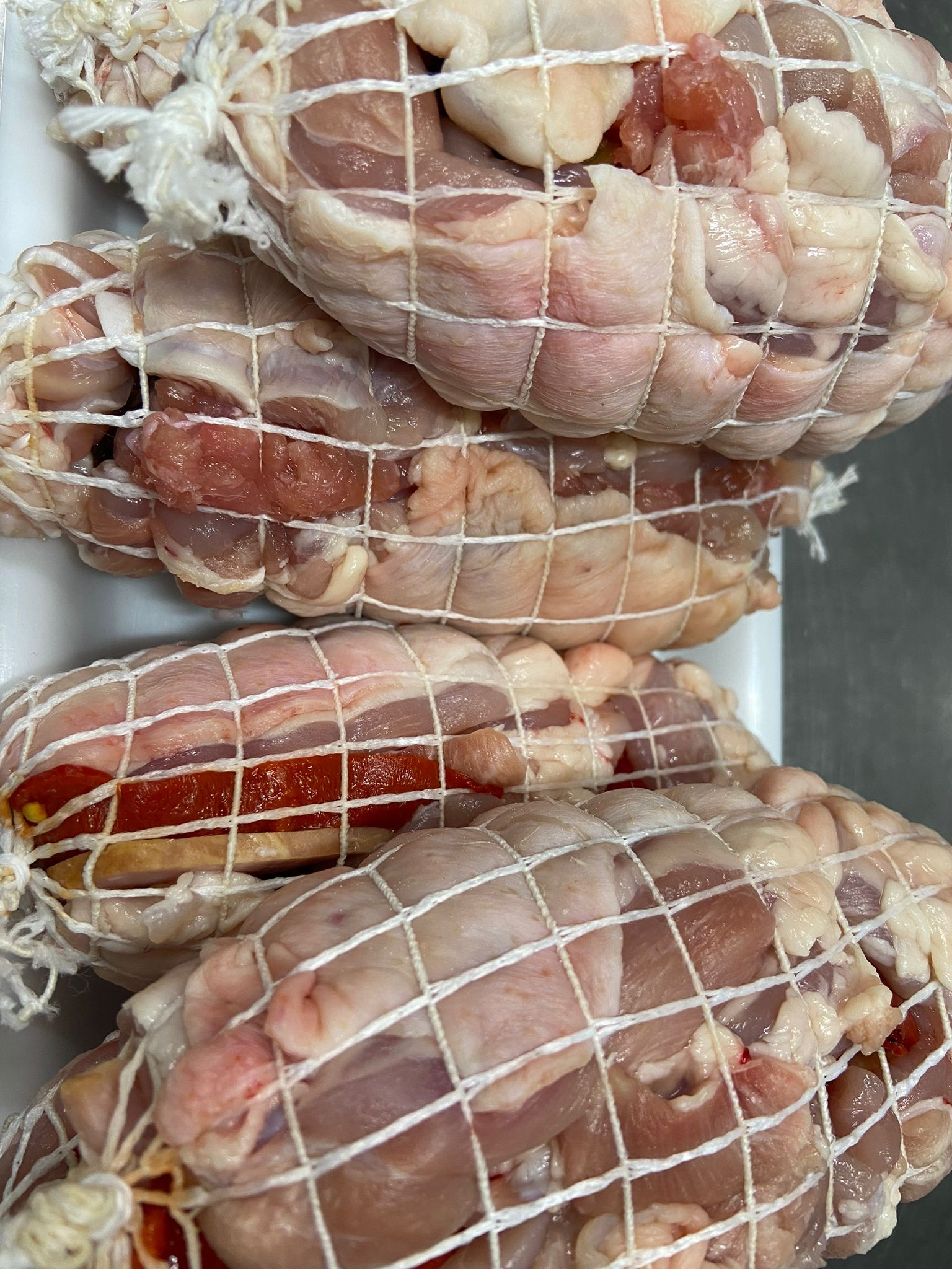 Carne cruda, envuelta en red, en una bandeja blanca.