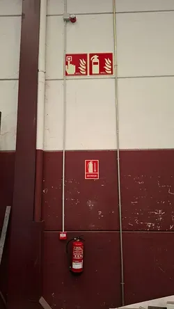 Extintor de incendios montado en la pared y señales de seguridad contra incendios en una pared industrial roja y blanca.