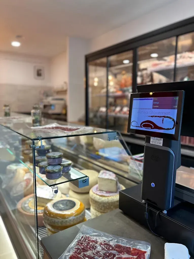 Vitrina con quesos y embutidos, puesto de caja con pantalla, interior de tienda.