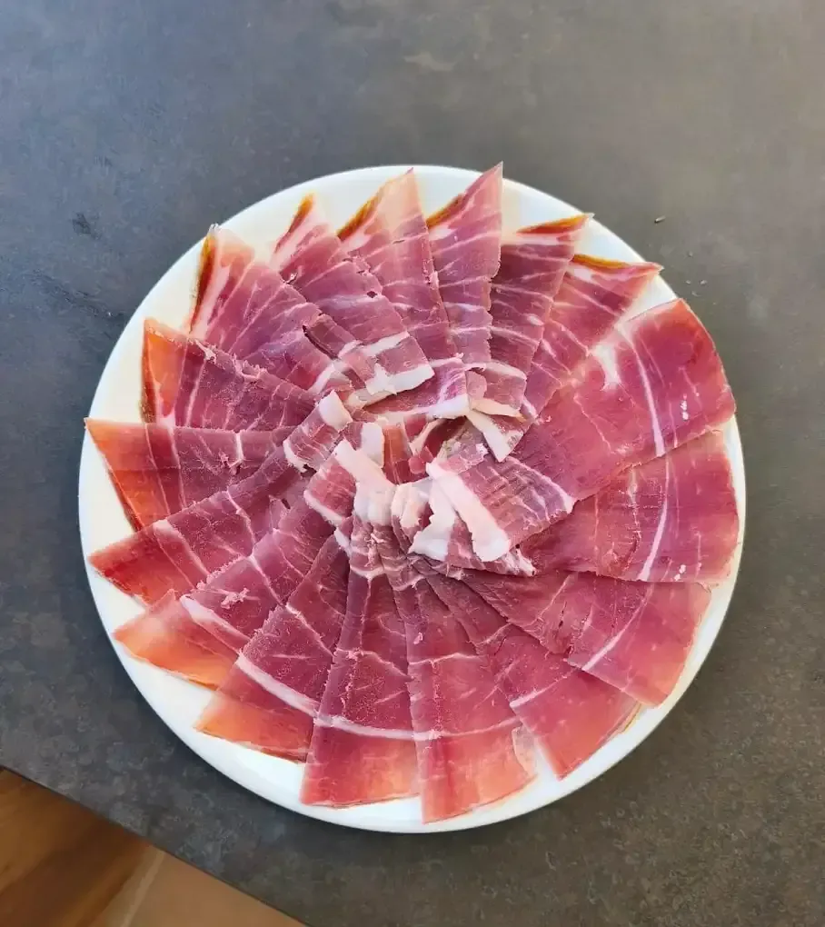 Plato de jamón curado cortado en lonchas finas y dispuesto en forma de espiral.