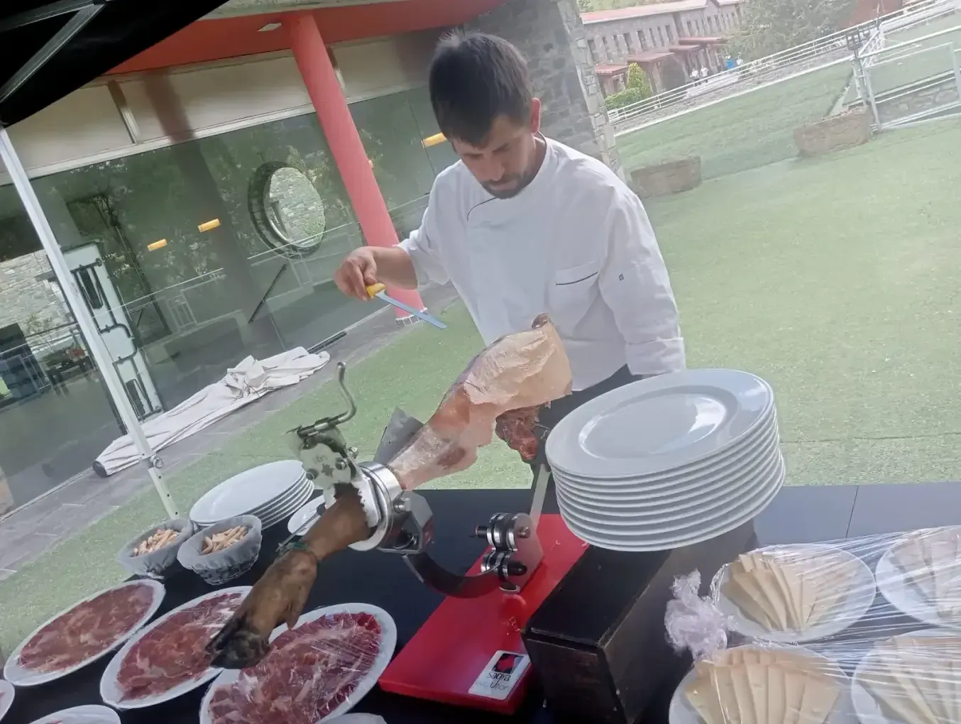 Chef cortando jamón curado en una mesa de buffet, preparando comida para una reunión.