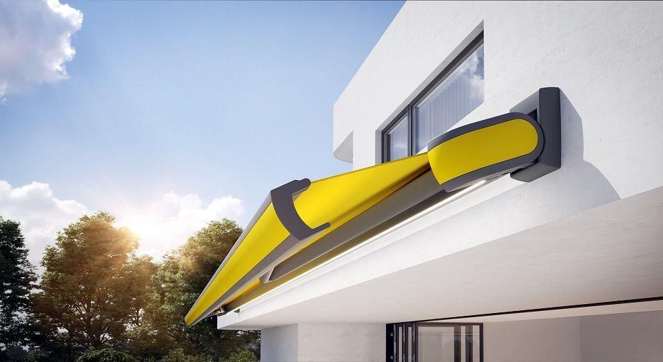 Eine gelbe, einziehbare Markise erstreckte sich von einem weißen Gebäude; im Hintergrund waren ein sonniger Himmel und Bäume zu sehen.