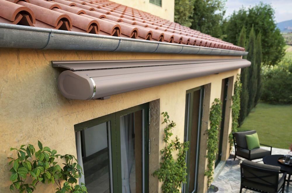 Beigefarbene Markise über den Fenstern eines verputzten Gebäudes mit rotem Ziegeldach.