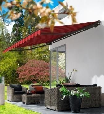 Eine rote, ausfahrbare Markise über Terrassenmöbeln neben einer weißen Wand, im Hintergrund ein Garten.