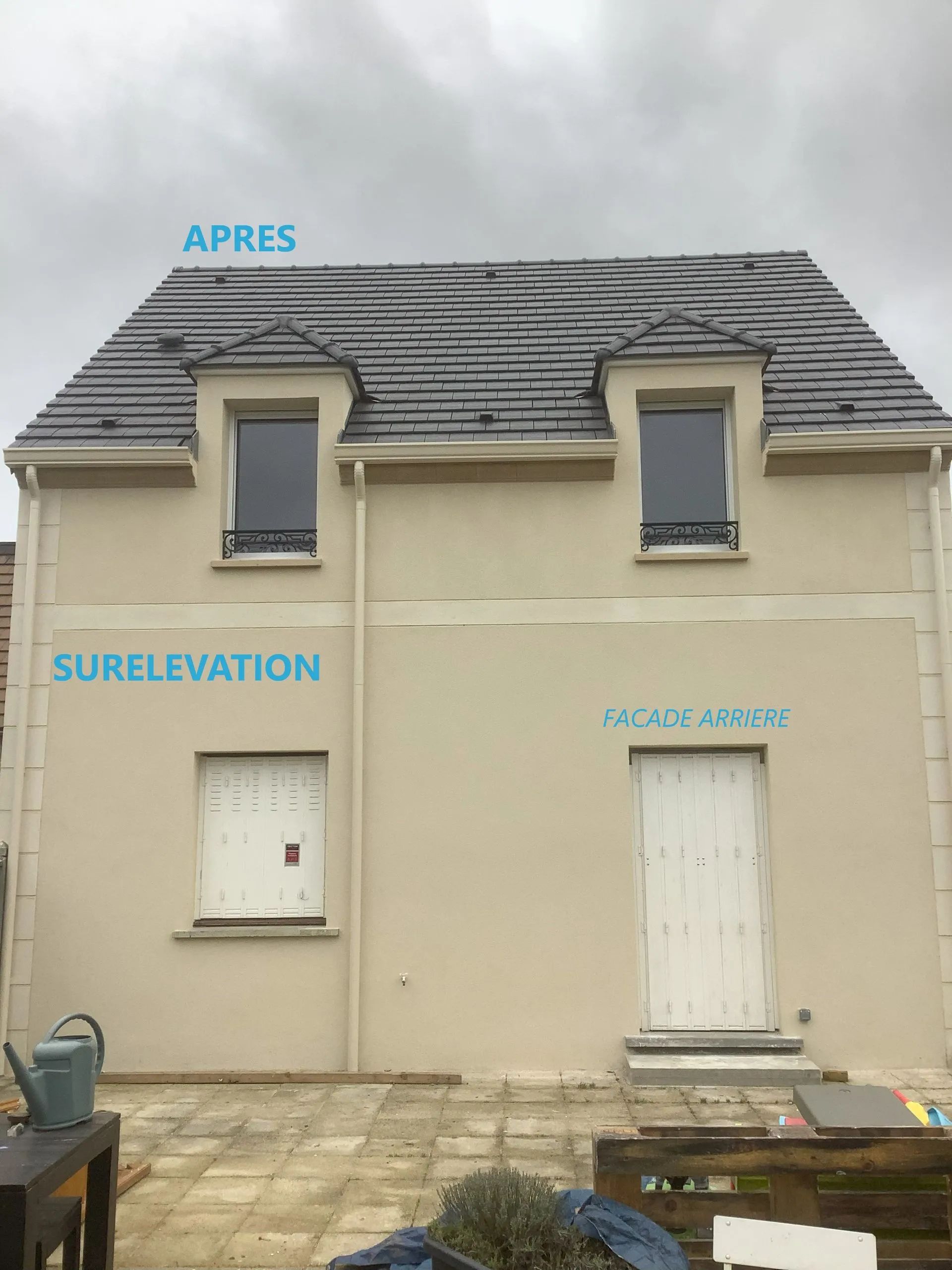 Extérieur de la maison après rénovation, avec deux lucarnes et une façade beige clair.