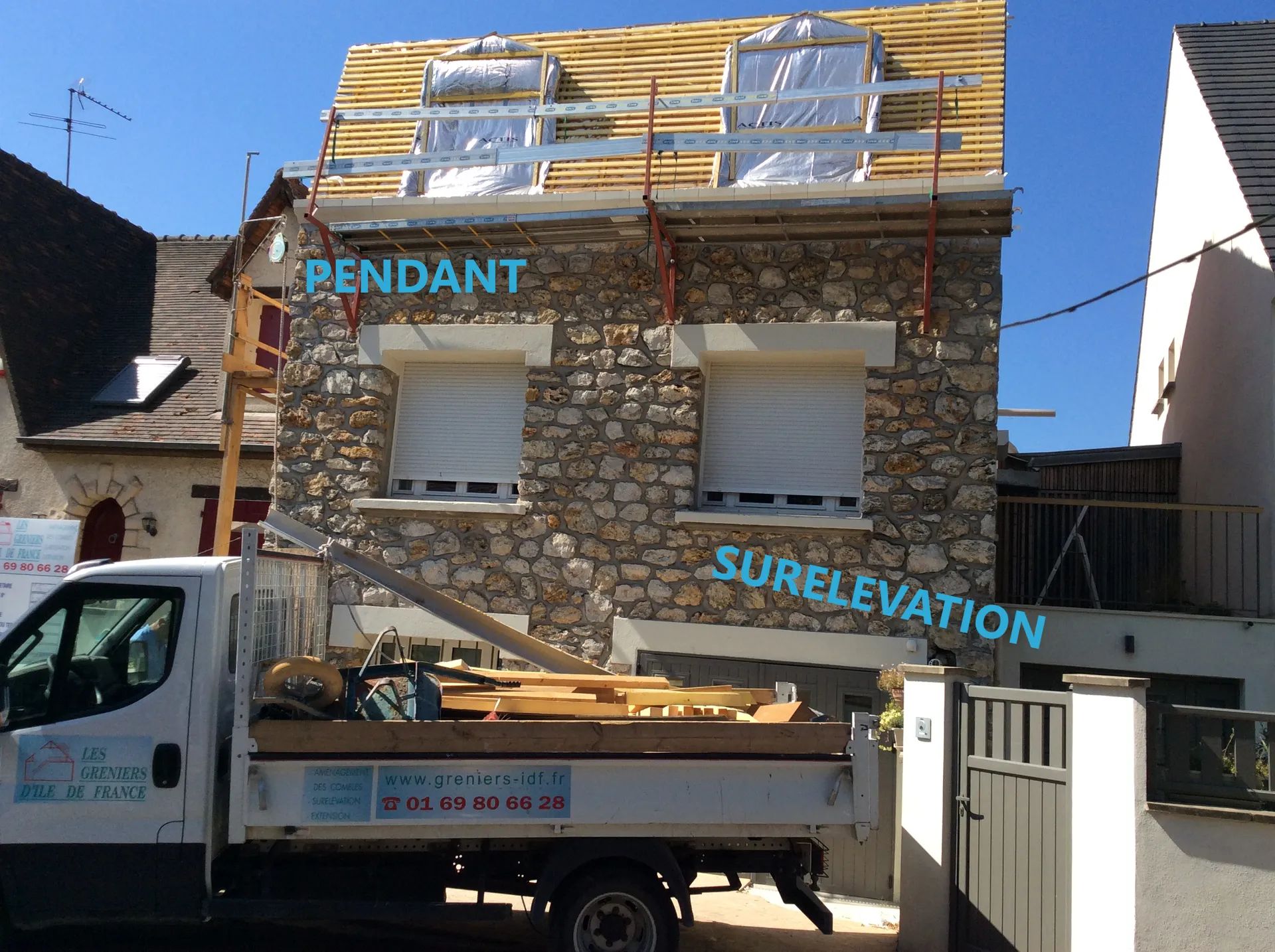 Maison à façade en pierre en cours de travaux d'extension de toiture ; camion garé devant.