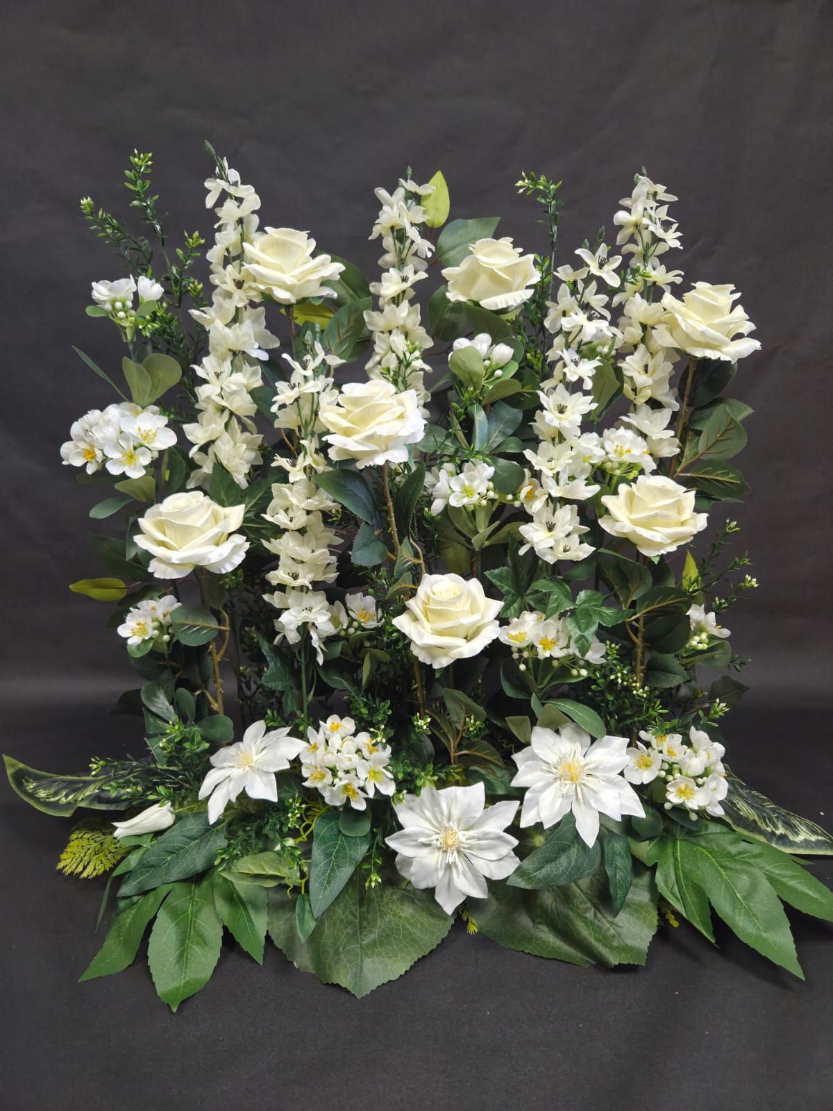 Une composition florale haute et dense, composée de roses crème et blanches, de poinsettias et de tiges verticales, sur fond noir.