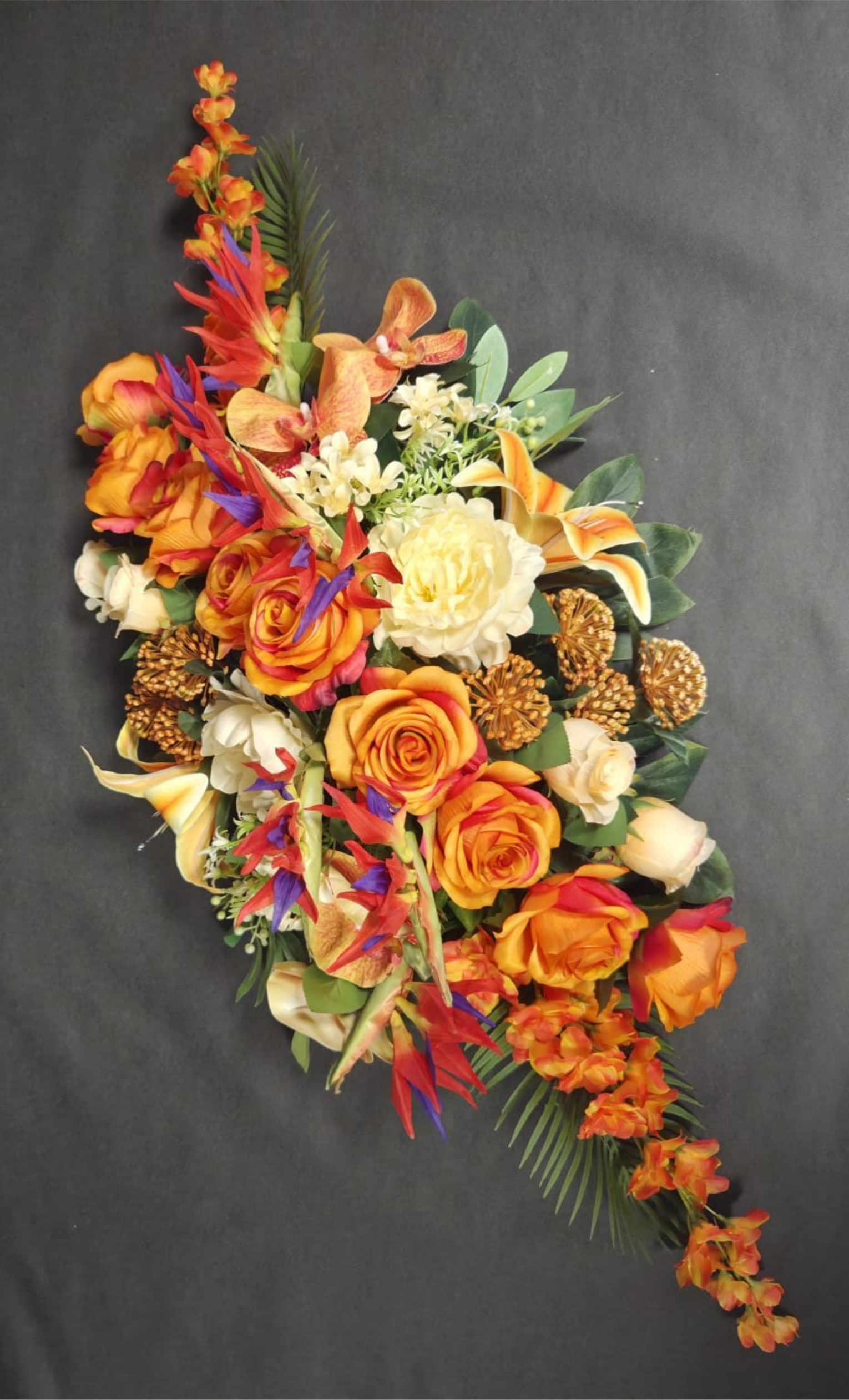 Une composition florale allongée mettant en scène des roses orange, jaunes et crème avec des touches de violet sur un fond sombre.