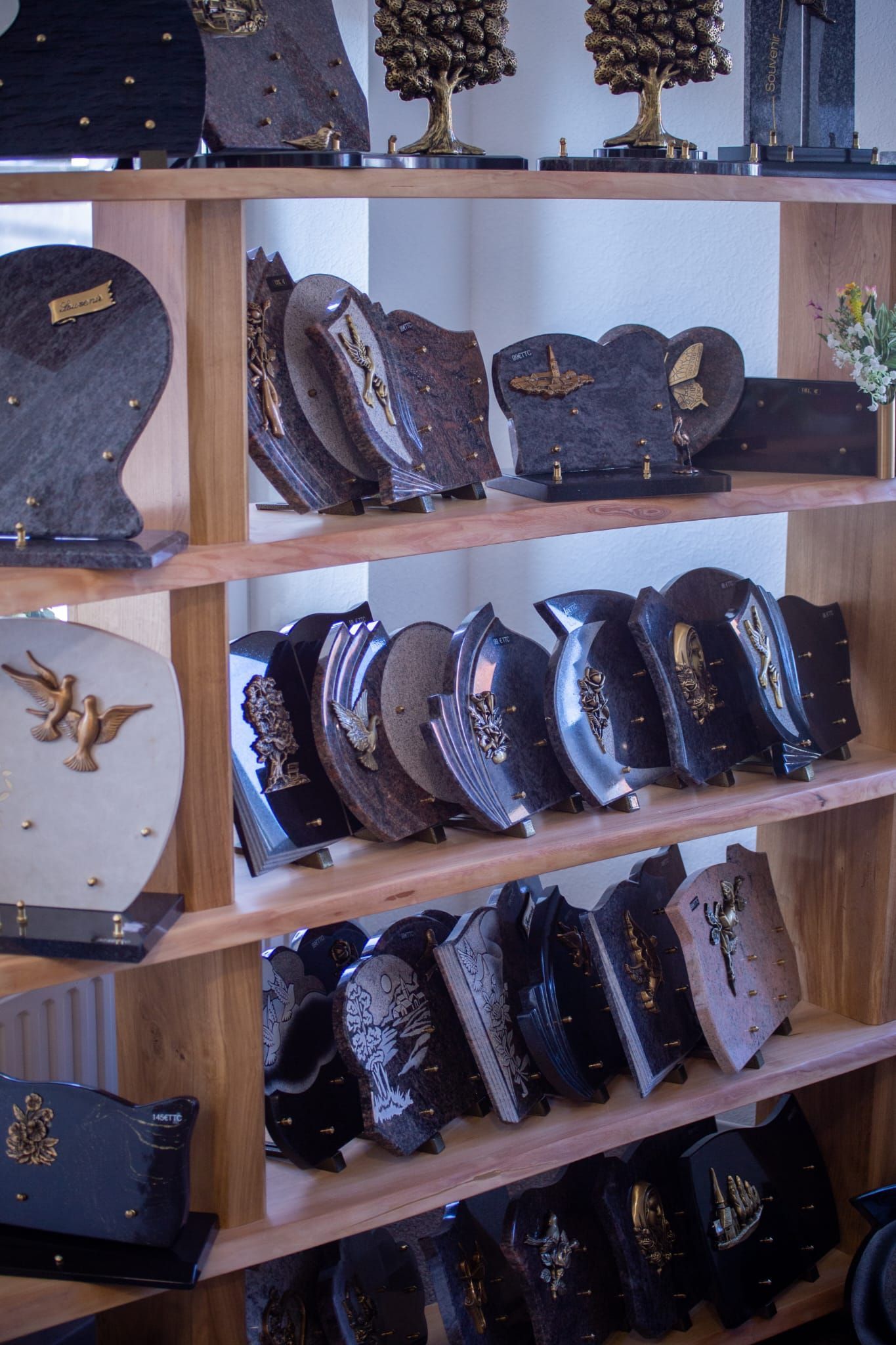 Une étagère en bois remplie de diverses plaques commémoratives sombres et gravées, ainsi que de petites pièces sculpturales.