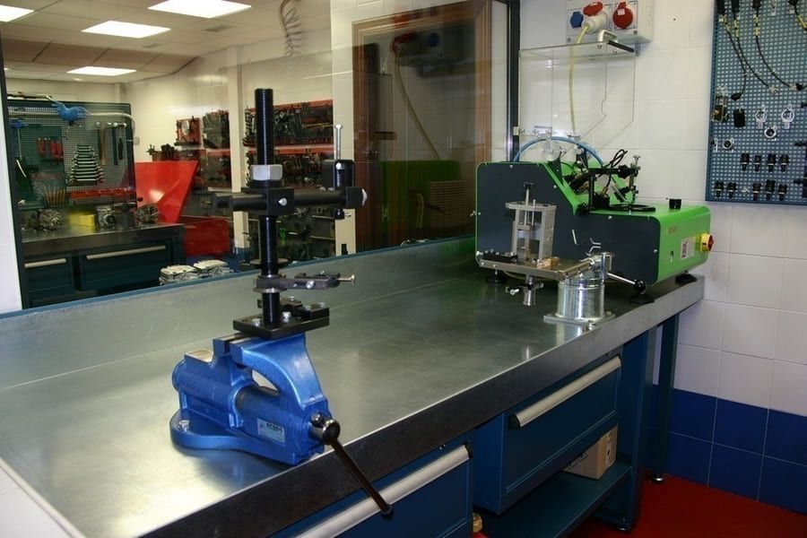 Un tornillo de banco azul se encuentra sobre una mesa de metal en un taller.