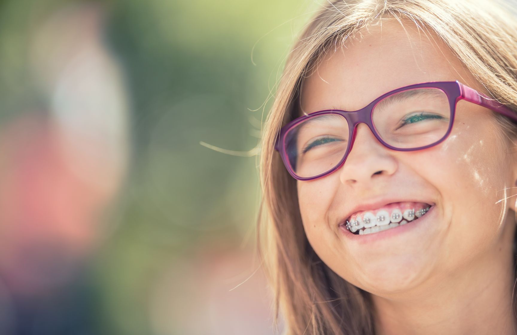 Petite fille qui sourit avec un appareil dentaire et des lunettes rouges.