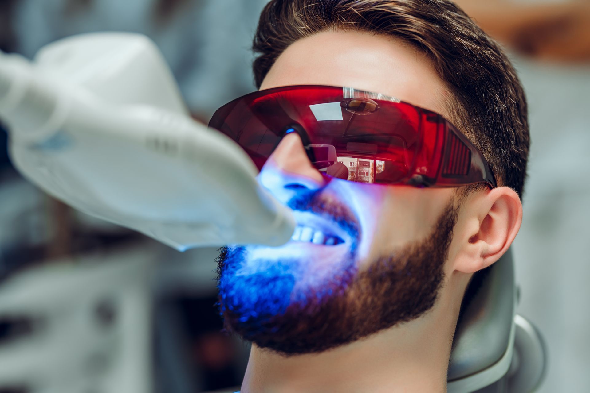 Dentiste qui applique une lumière bleue pour blanchir les dents d'un patient.